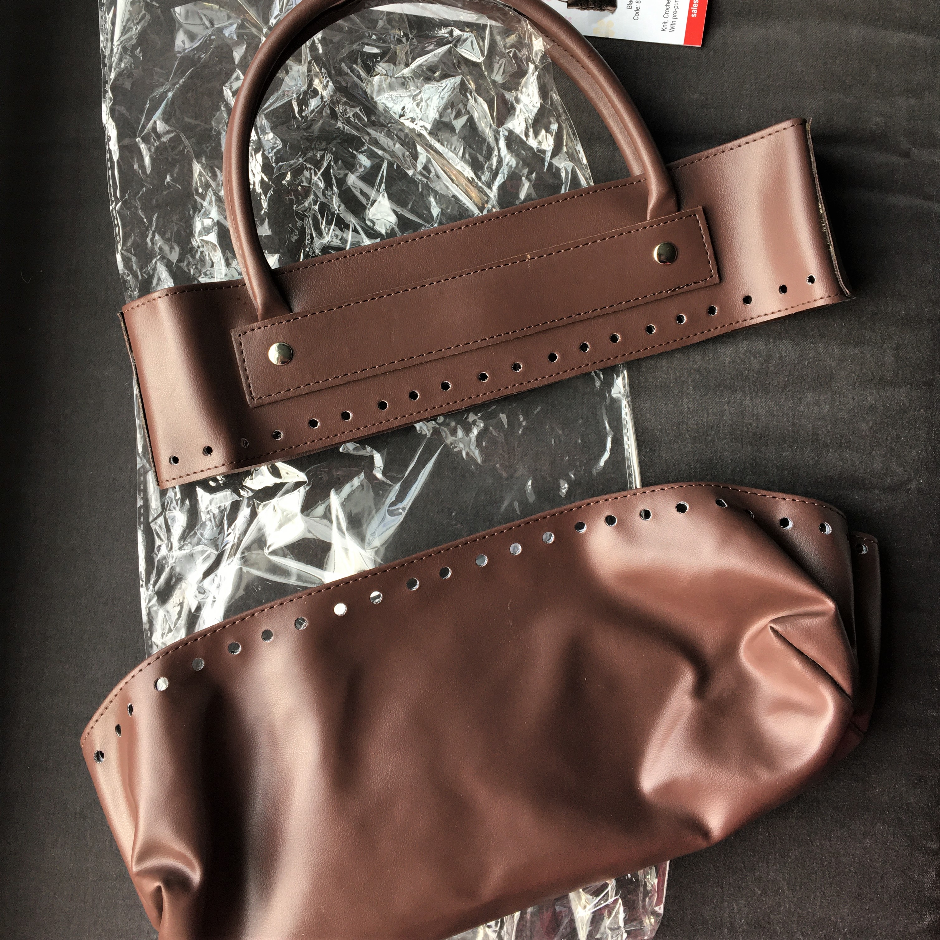 Brown pleather bag top and bottom against plastic shipping bag and a grey background.